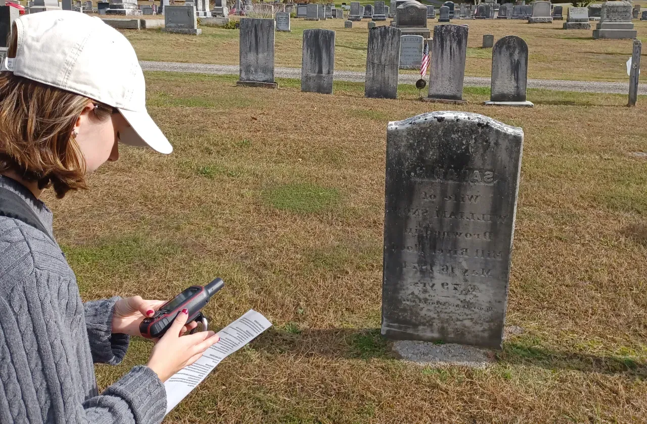 A student holds a tracking device in a cemetery.